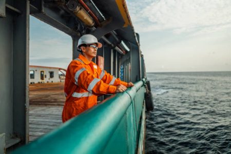 Filipino deck Officer on deck of vessel or ship , wearing PPE personal protective equipment - helmet, coverall, lifejacket, goggles. Safety at sea. He is tired